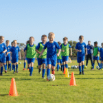 Young players dribbling around cones at a Bonnet Bay FC Bombers Academy soccer clinic on a sunny field