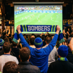 A crowd of Bonnet Bay FC fans watching the World Cup on the big screen at The Hangar, with a blue and green Bombers scarf held up in the crowd