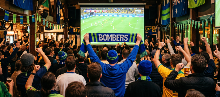 A crowd of Bonnet Bay FC fans watching the World Cup on the big screen at The Hangar, with a blue and green Bombers scarf held up in the crowd